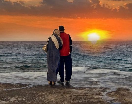 A man and woman standing on the beach at sunset.